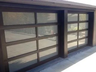  Two modern glass-panel garage doors with wooden frames on a residential property.