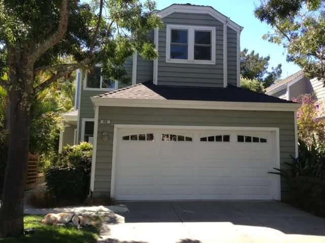  A grey two-story house with a white double garage door and surrounding trees.