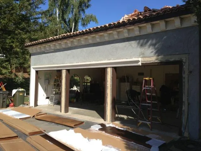 A partially open garage with two ladders and construction materials around. Workers are inside, and boards are on the ground outside.