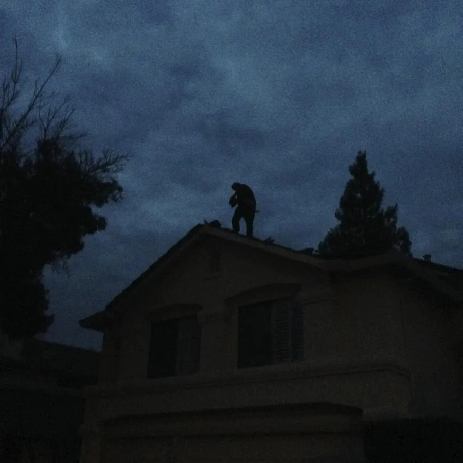  A person standing on a rooftop silhouetted against a dark, cloudy sky, working on the roof of a house.