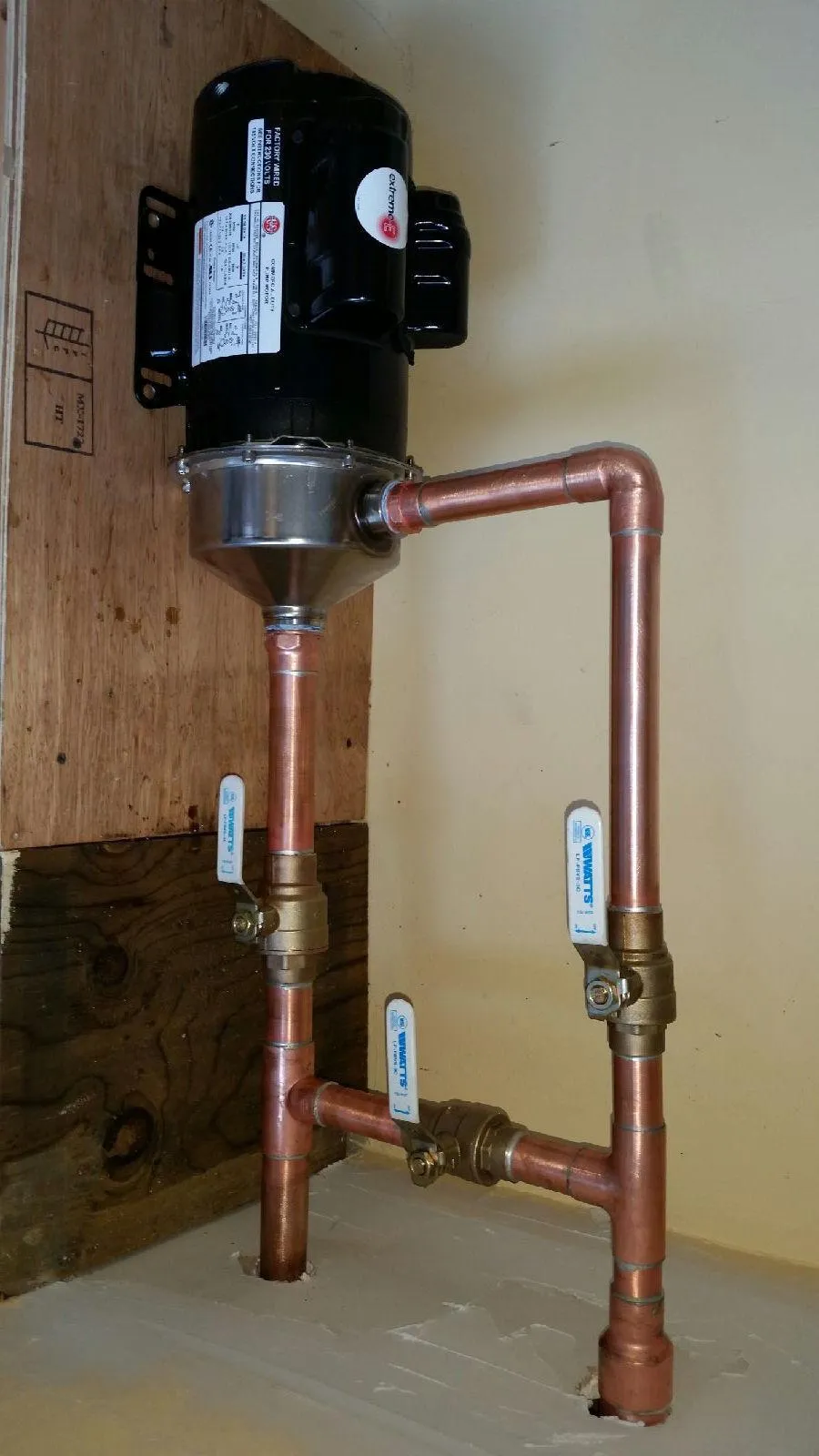  Copper pipes are installed with precision, featuring valves and a black motor, mounted against a wooden and plastered backdrop.