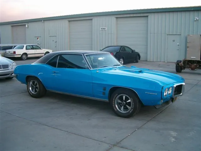  A blue vintage car parked in front of a row of garage doors at an auto repair shop.