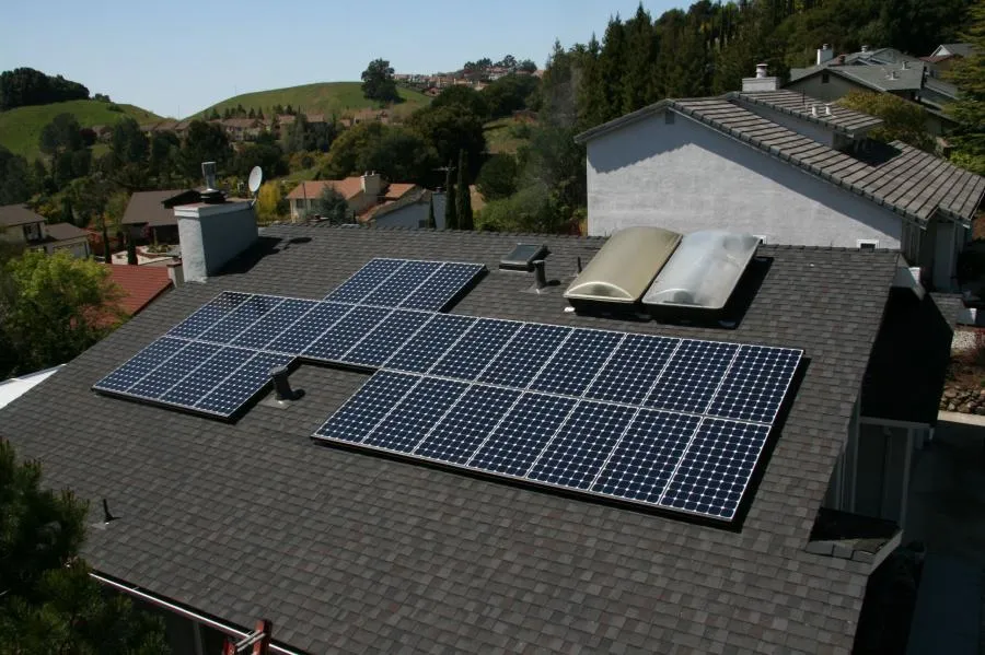  Solar panels installed on a house roof, surrounded by greenery and neighboring homes.