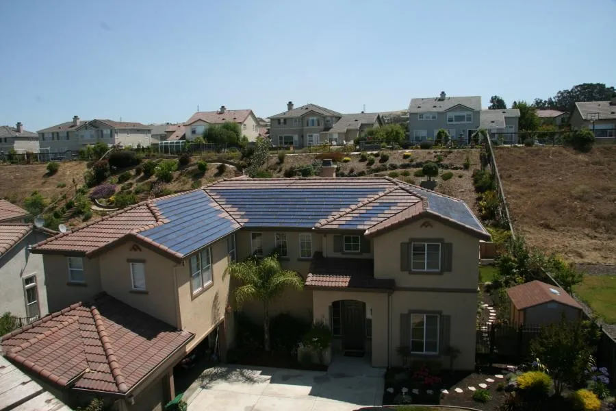 A suburban house with solar panels on the roof, surrounded by a garden and similar neighboring houses.