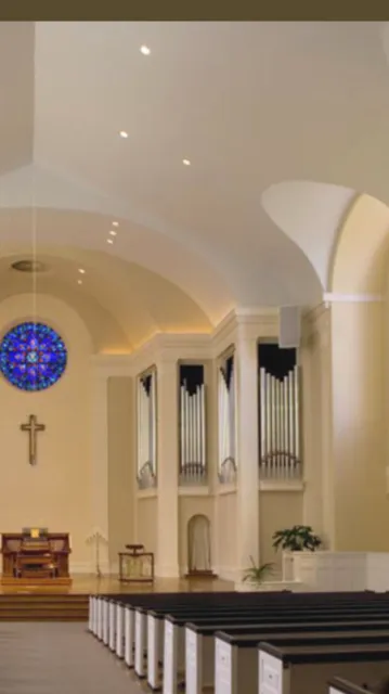  Interior view of a church with a high arched ceiling, stained glass window, organ pipes, and wooden pews.