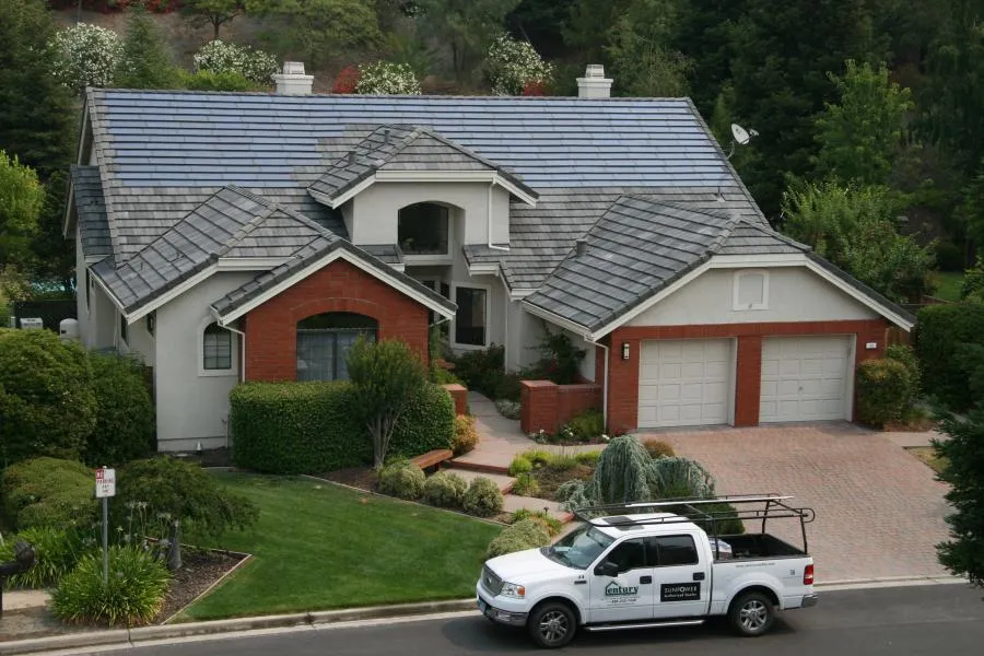  House with a new slate-style roof, surrounded by lush landscaping. A Century Roof and Solar truck is parked on the driveway.