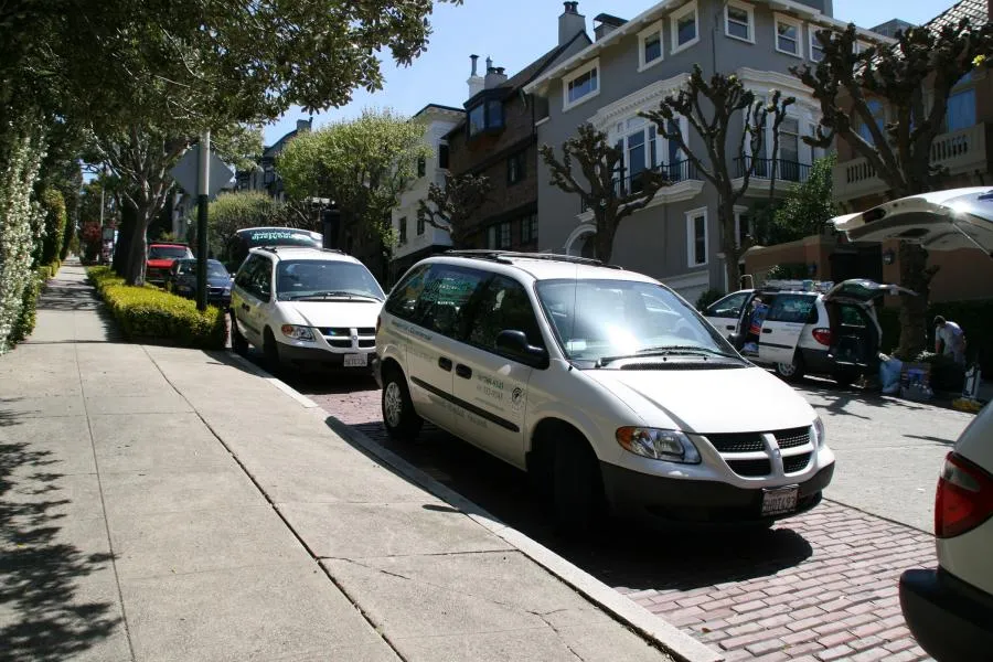  White vans from SonoMarin Cleaning Services parked along a residential street with trimmed trees and brick sidewalks.