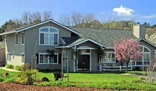  A large two-story house with a gray roof, white trim, and a blooming cherry tree in the yard.