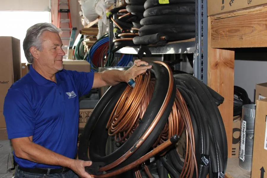 Picture of In a neatly organized storeroom, an employee of Moore Mechanical Heating & Air Conditioning carefully selects a coil of copper tubing, symbolizing the company's dedication to quality outcomes. Copyright ©2025 Diamond Certified Resource - Moore Mechanical Heating & Air Conditioning