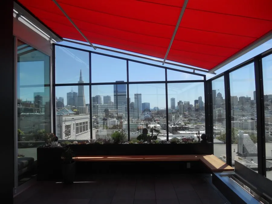  Rooftop view with a red awning, glass walls, and city skyline in the background.