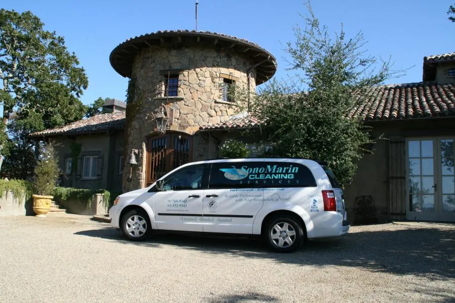  White SonoMarin Cleaning Services van parked in front of a stone building with a circular tower and tiled roof.