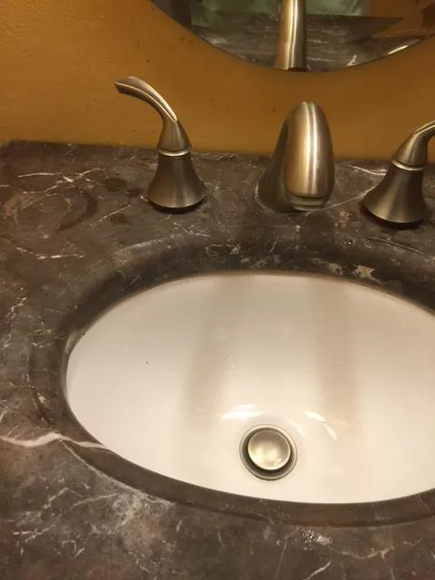  Close-up of a marble sink countertop with a shiny faucet and two handles.