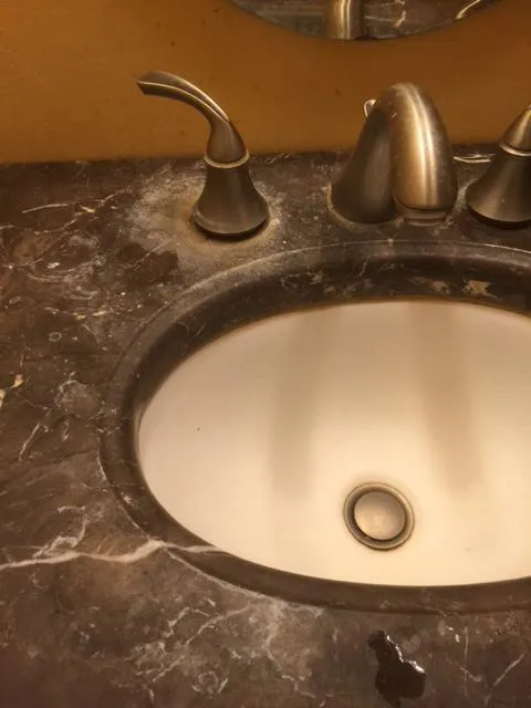  Close-up of a marble countertop with a clean sink and stainless steel faucet.