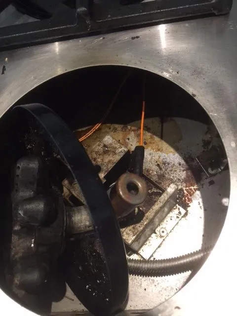  Close-up of a commercial kitchen stove's internal components, showing a circular opening with wires and mechanical parts.