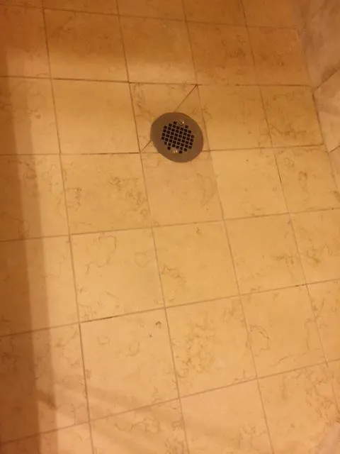  Close-up of a tiled floor with a circular metal drain at the center.