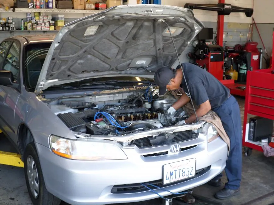  Technician working on an open Honda engine in an auto repair shop, surrounded by toolboxes and shelves with supplies.