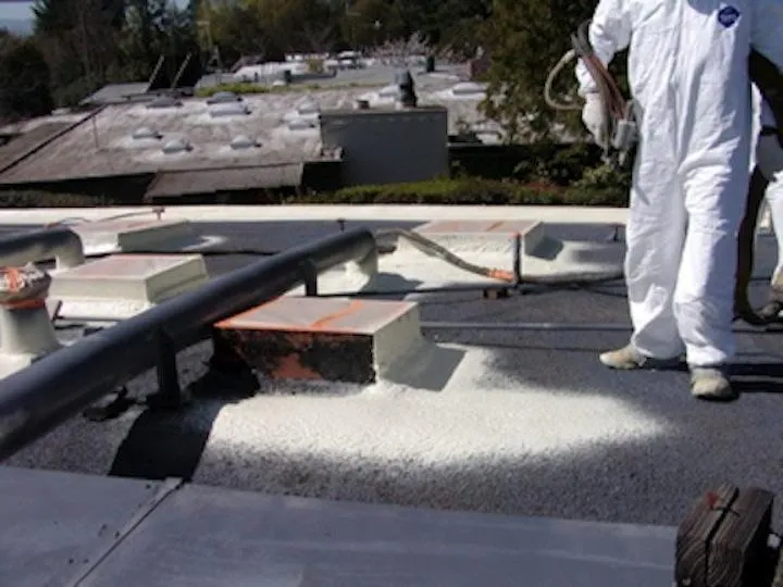  A person in protective gear applies roofing material to a flat roof, surrounded by ventilation structures and piping.