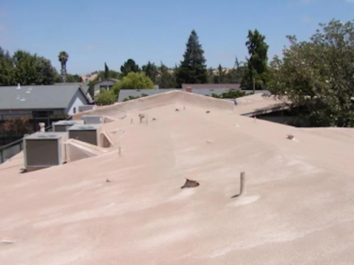  Flat beige roof with protruding vents and nearby trees, under a clear sky.