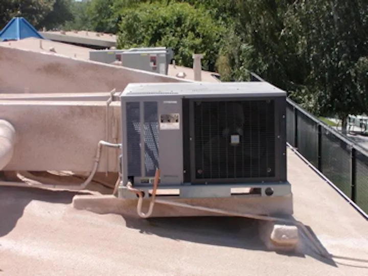  Rooftop view with an air conditioning unit installed on a flat surface, surrounded by trees and a fence.