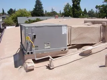  Rooftop view of a flat roof with an installed air conditioning unit and visible piping. Trees and a building are in the background.