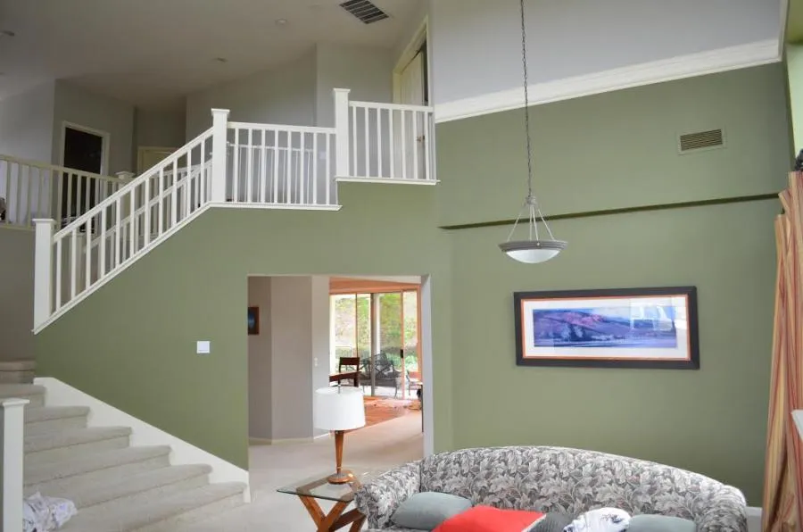  Interior space with an olive green accent wall, white staircase railings, a hanging light fixture, and a landscape painting above a patterned sofa.