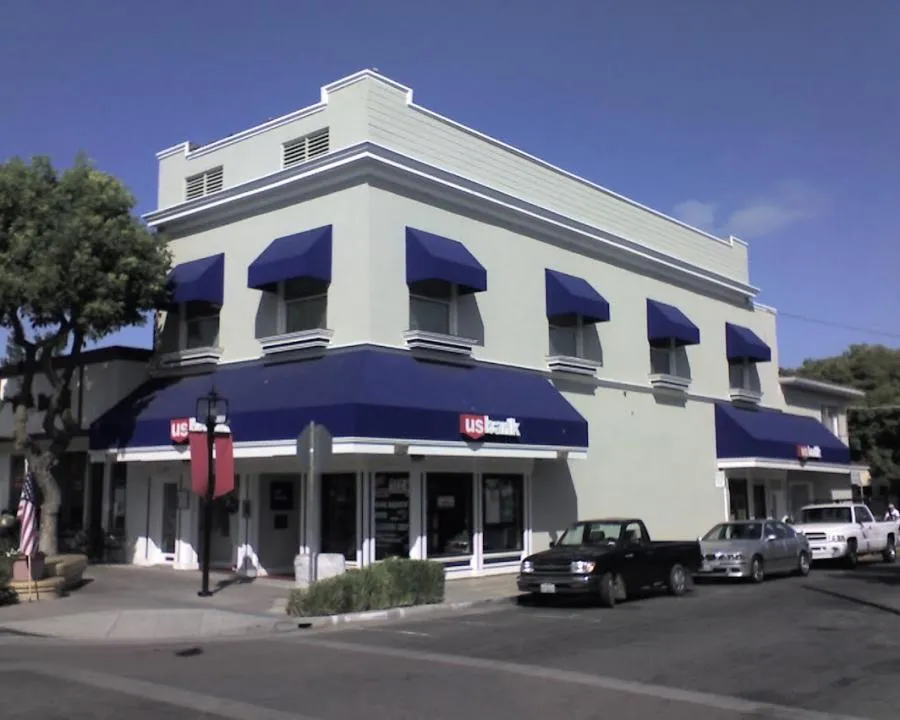 A building with blue awnings on a sunny day, featuring a "US Bank" logo, and parked cars nearby.