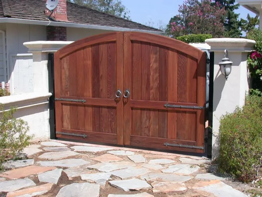  Wooden double gate with arch design, flanked by white columns and stone pathway in front.