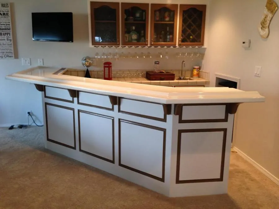  A home bar with wooden trim, cabinet, countertop, glass rack, and wall-mounted TV.