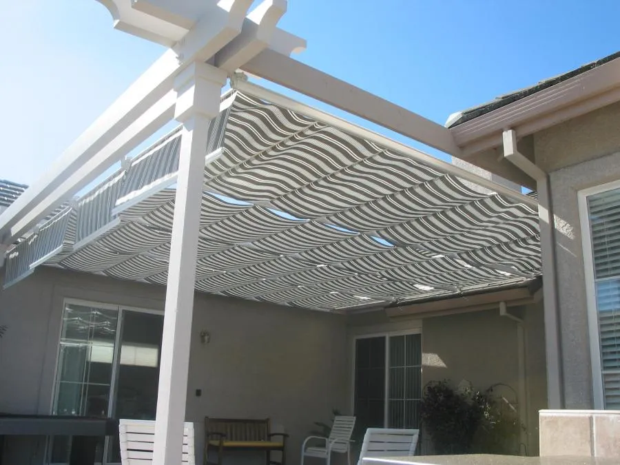 Striped retractable awning extends over a patio with outdoor furniture, attached to a house's siding.
