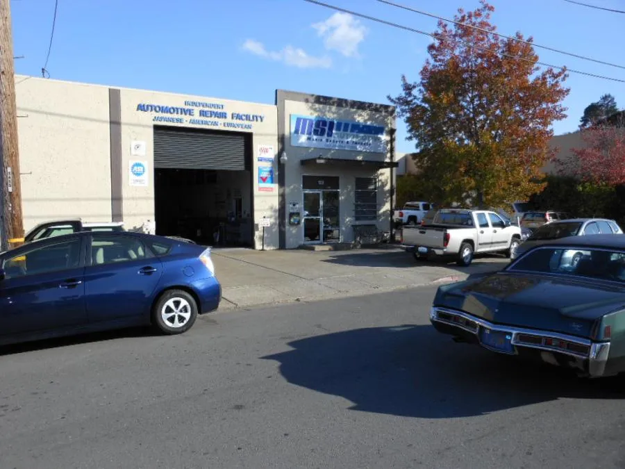 Exterior of MSI Automotive Repair Facility with several cars parked outside, including a classic car and a modern sedan. The open garage door and signage are visible.