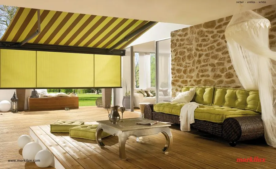 Outdoor patio with retractable yellow and green striped awning, wicker seating with green cushions, wooden deck, and stone wall.