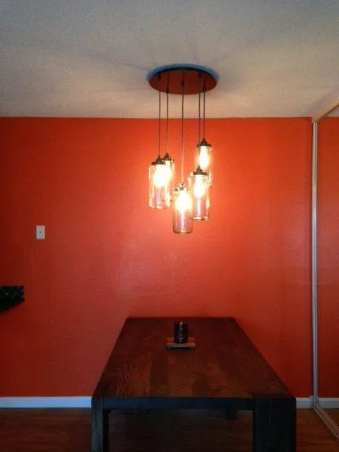 Hanging light fixture with multiple bulbs over a wooden table against an orange wall.