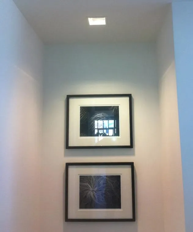  Two framed artworks in a small, lighted alcove with a ceiling light above.
