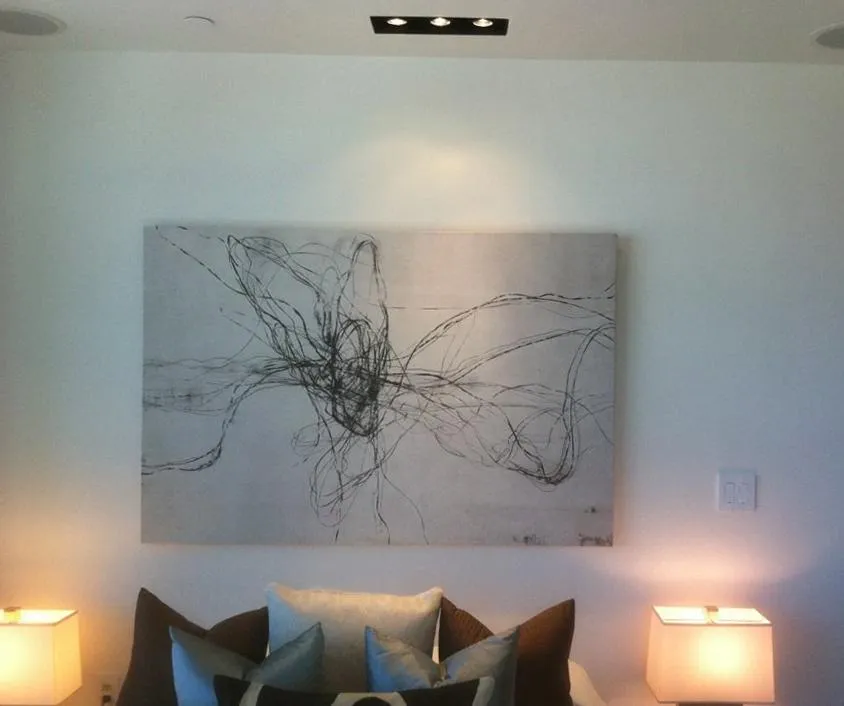 Abstract painting on wall above a couch with pillows, flanked by two illuminated lamps in a softly lit room.