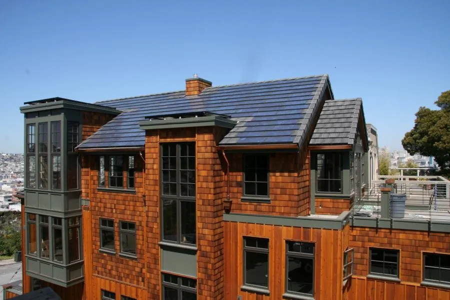  A building with wooden siding and dark-framed windows features solar panels installed on its roof under a clear blue sky.