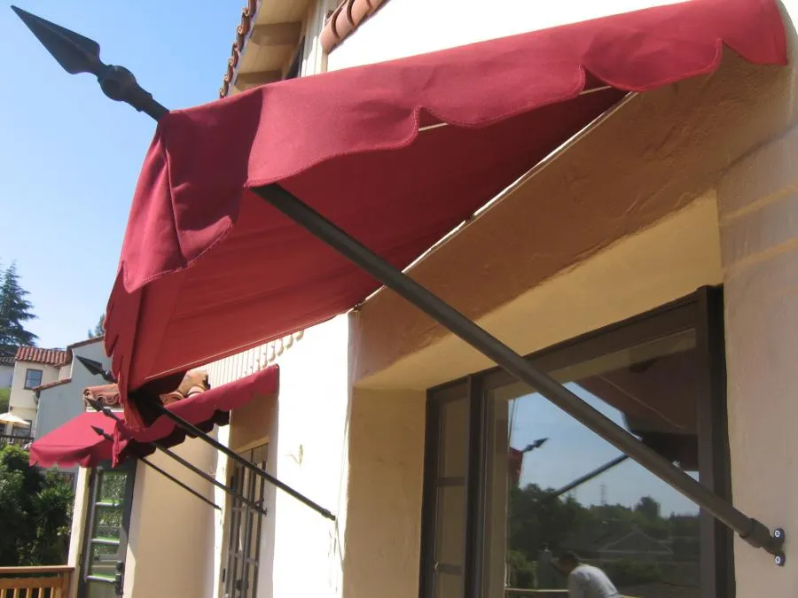  Red fabric awning with spear-like metal supports attached to the exterior wall above a window.