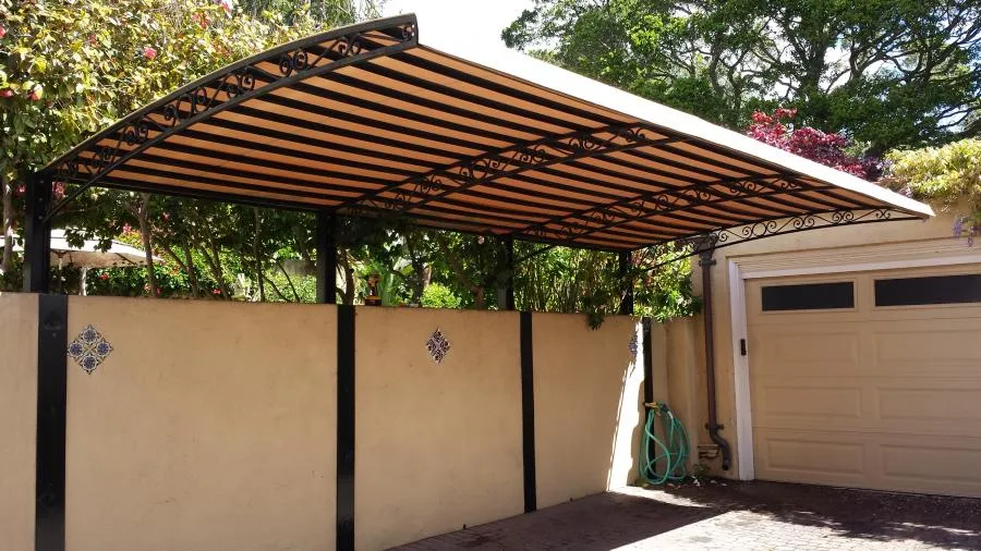  Striped sunshade with intricate designs over a patio, attached to a garden wall near a garage.