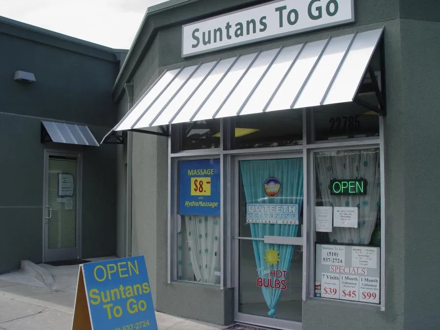  A storefront with a sign reading "Suntans To Go," featuring advertising for massages and UV teeth whitening. An open sign is visible on the window.