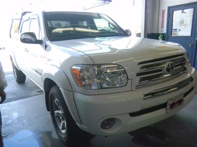 White pickup truck in a garage, partially visible with workshop lights reflecting on its surface.