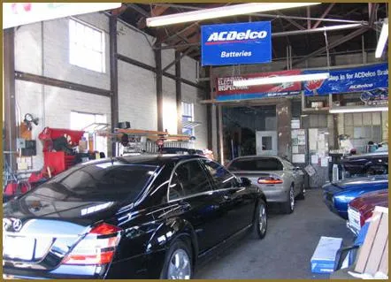 Interior of an auto care center with several cars parked in service bays, tools and equipment visible, and an ACDelco Batteries sign hanging above.