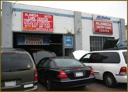  Several cars parked in front of Alameda Auto Care Center, an auto service garage with a sign indicating it's an official smog station.