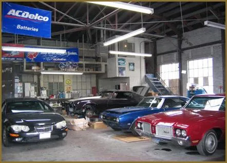  A variety of classic and modern cars are parked inside a well-lit auto care center with ACDelco signage hanging above.