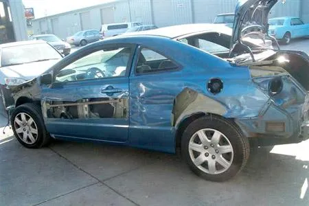  A blue car with damaged and stripped panels parked, awaiting repair in an auto repair lot.