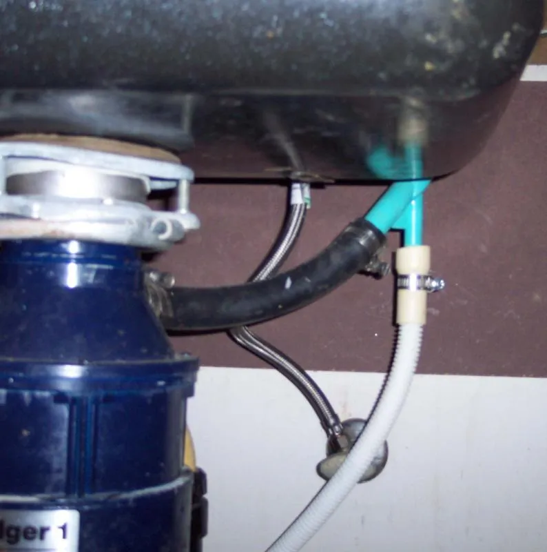 Close-up of plumbing under a kitchen sink, showing a disposal unit connected to various pipes and hoses.