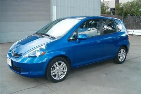 Blue hatchback car parked on a concrete surface outside a building with gray siding.