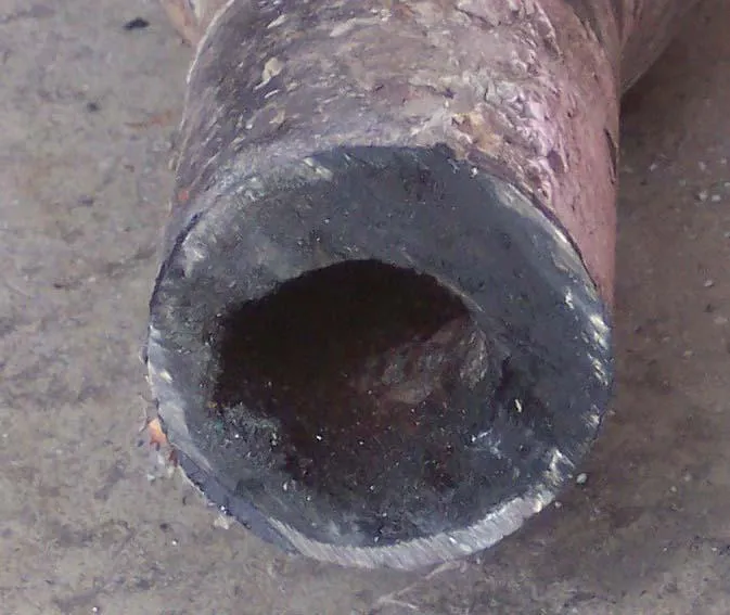  Close-up of a corroded pipe with visible buildup, lying on a concrete surface.