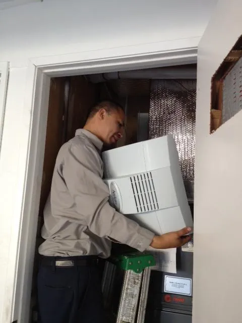 Picture of A technician from Qualtech Heating & Cooling expertly installs a new air filtration unit in a compact space, highlighting the company's commitment to quality outcomes. Qualtech consistently achieved a Highest in Quality rating, ensuring installations meet superior standards. Copyright ©2025 Diamond Certified Resource - Qualtech Heating & Cooling