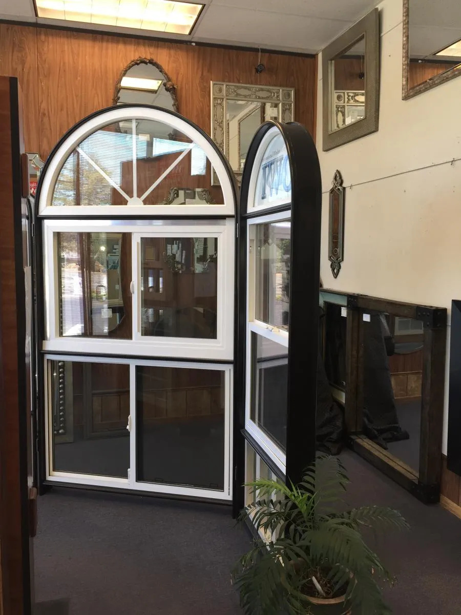Indoor showroom featuring arched and rectangular windows, surrounded by framed mirrors on wooden panel walls, with a potted plant in the foreground.