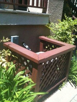  Enclosed outdoor HVAC unit with surrounding plants and a wooden lattice structure.