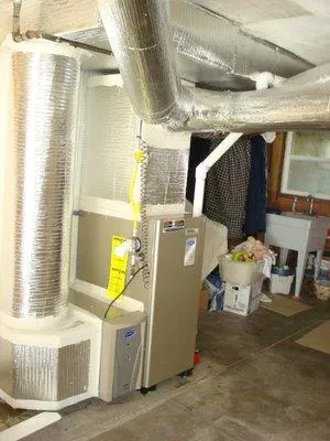 Basement with newly installed HVAC system and silver ductwork beside utility shelves and a sink.